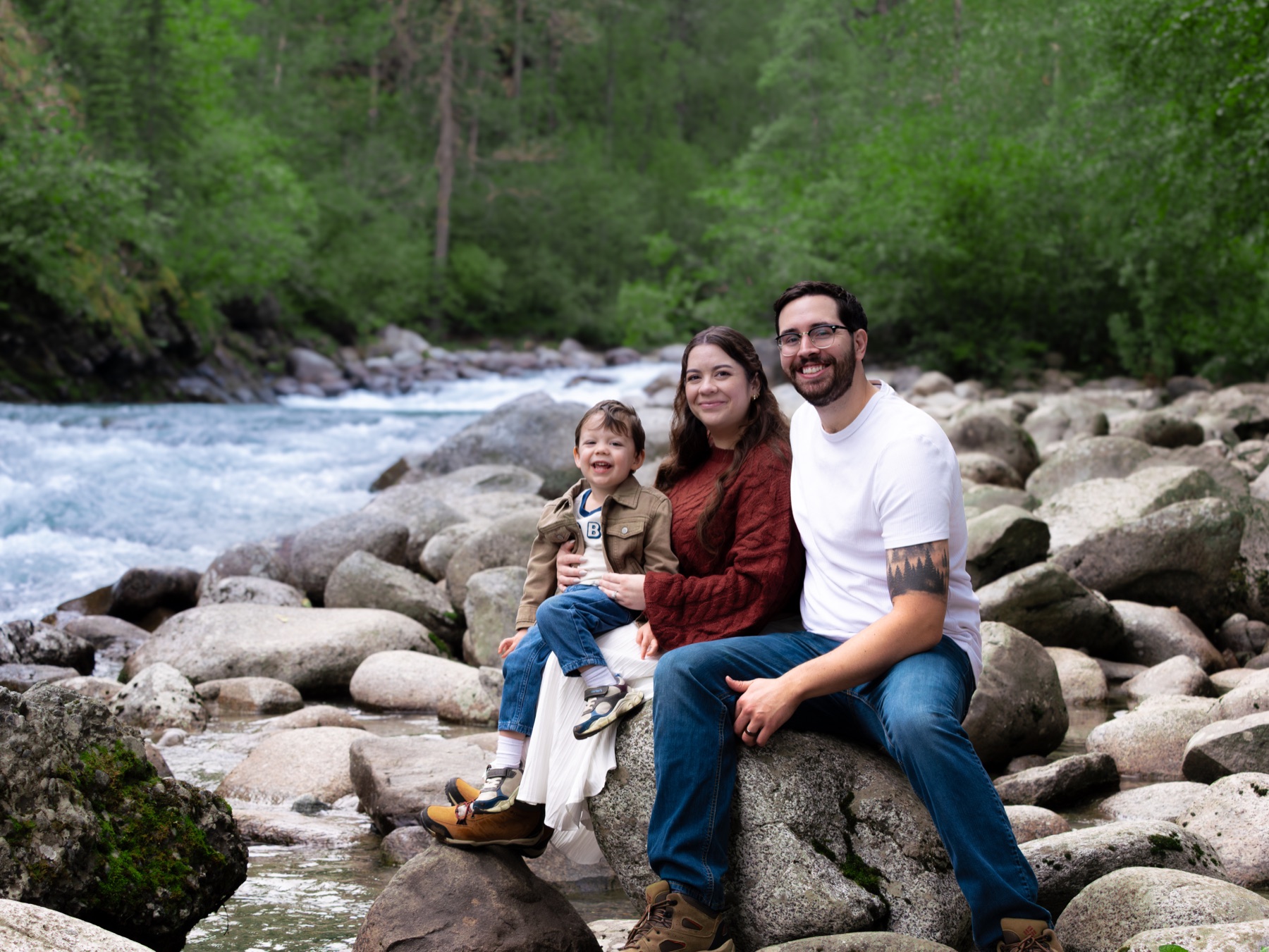Hannah and Kenny with their young child seated on rocks beside a flowing creek near Hatcher Pass, Alaska
