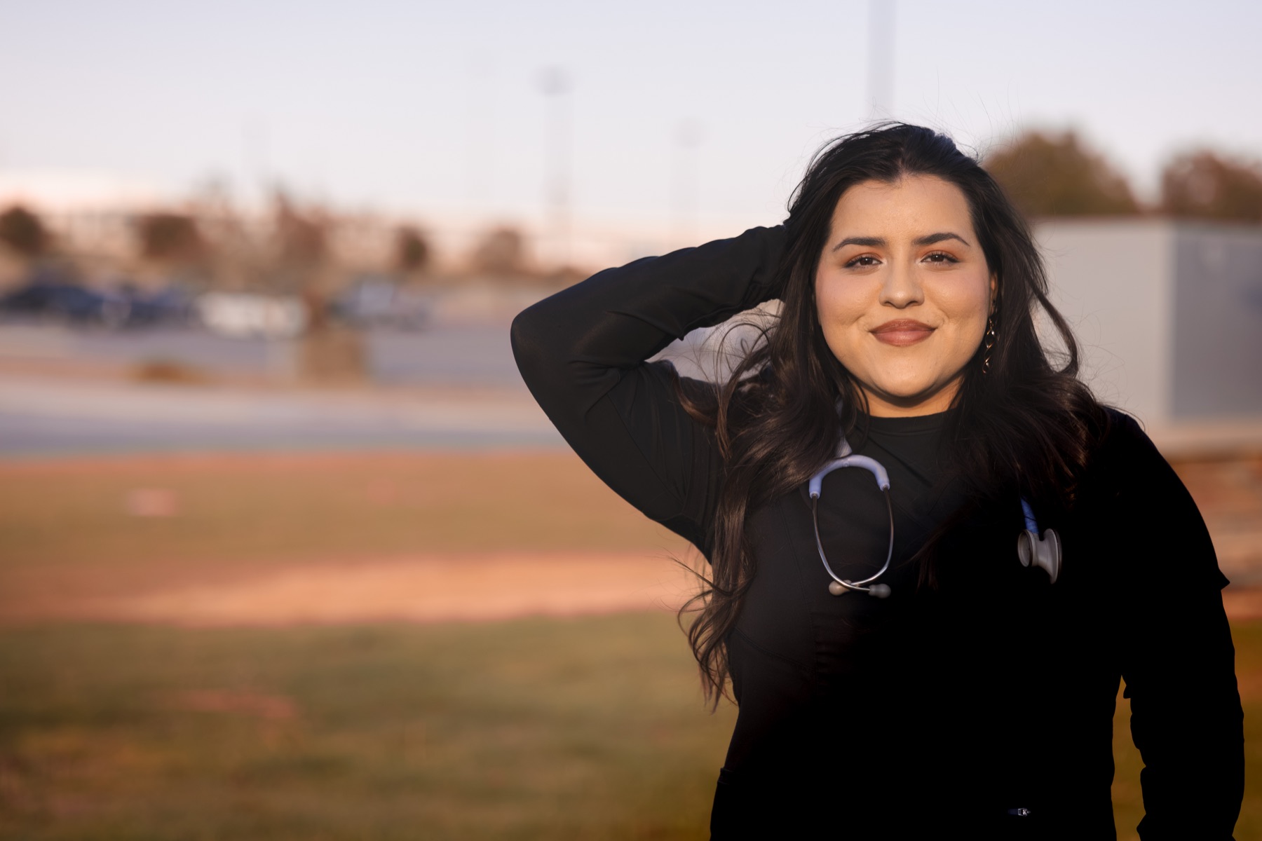 Celeste looking toward the camera outdoors in black scrubs
