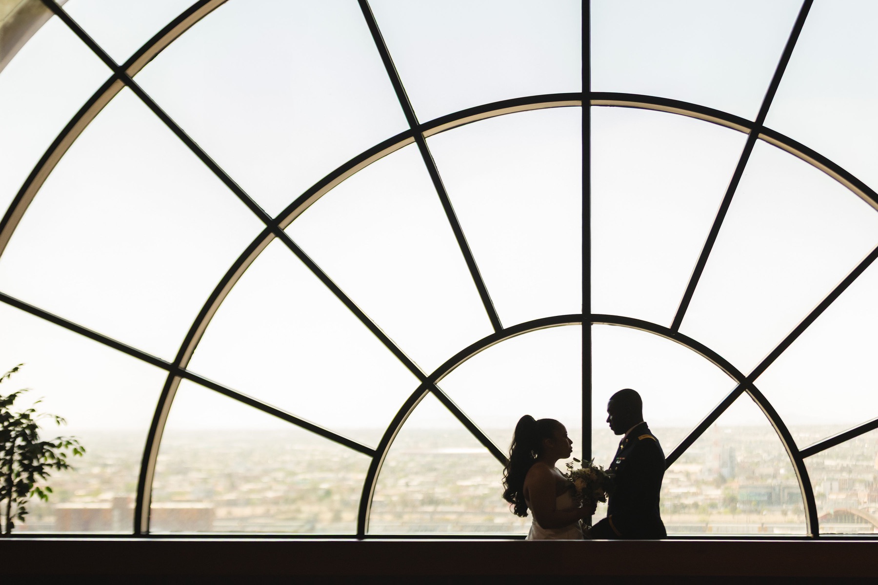 Newlyweds silhouetted beneath a large arched courthouse window